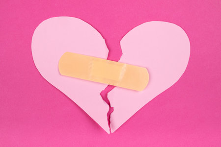 Torn paper pink heart with beige adhesive bandage. Healed broken heart conceptの写真素材