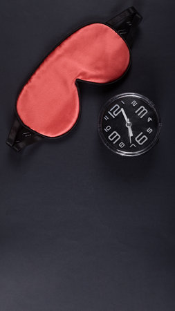 Red sleeping mask and alarm clock isolated on dark grey background. World sleep day concept