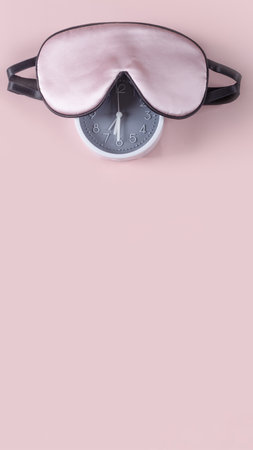 Light pink sleeping mask and alarm clock isolated on pastel pink background. World sleep day conceptの写真素材