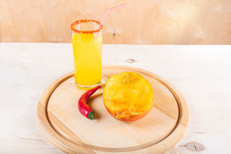 Glass of mangonada, half of mango and red hot chili pepper on wooden backgroundの写真素材