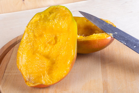 Side view of two halves of mango and kitchen knife on wooden backgroundの写真素材