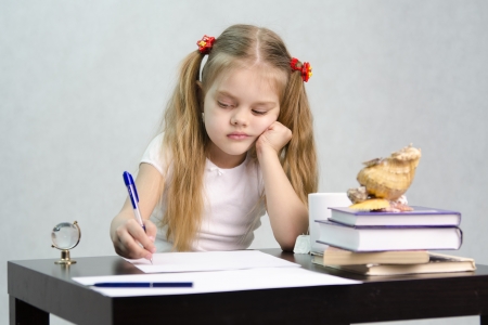The girl writes on a piece of paper sitting at the table in the image of the writerの写真素材