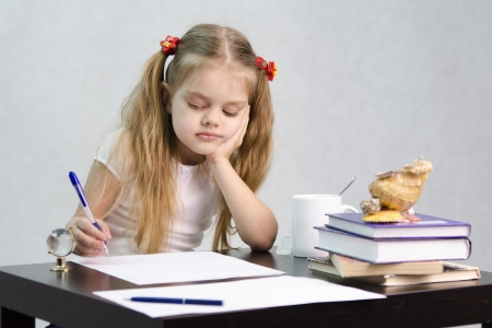 The girl writes on a piece of paper sitting at the table in the image of the writerの写真素材