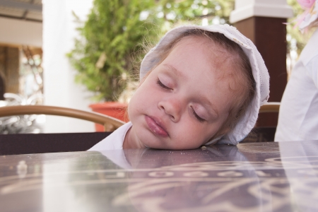 Two-year-old girl asleep at a table in the street cafeの写真素材