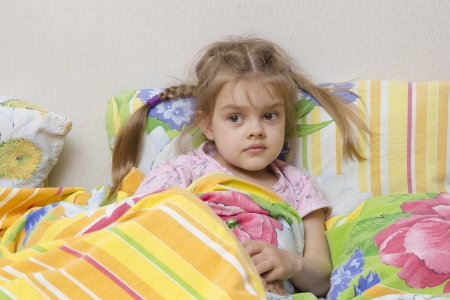 Four-year-old girl with pigtails lying in bed under the blanketの写真素材