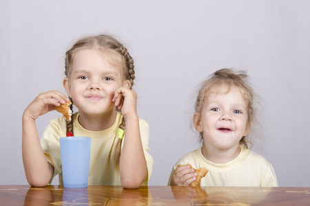 Two children sitting at the table, eating a muffin and drink of colored plastic cupsの写真素材