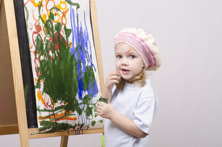 Three-year-old girl playing in the artist. Girl draws on the easel paintsの写真素材