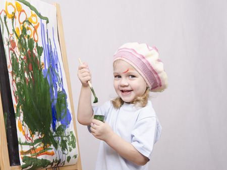 Three-year-old girl playing in the artist. Girl draws on the easel paintsの写真素材