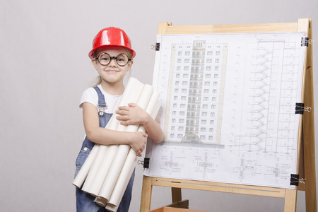 Girl Builder, architect, holding a bunch of drawings, standing at the blackboard with the drawing of the buildingの写真素材