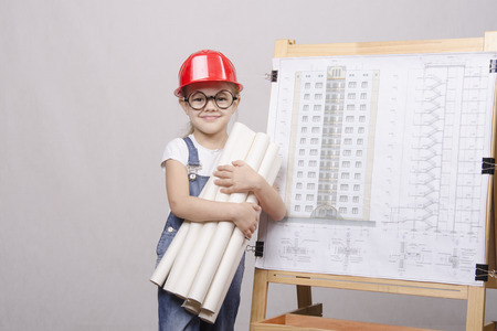 Girl Builder, architect, holding a bunch of drawings, standing at the blackboard with the drawing of the buildingの写真素材