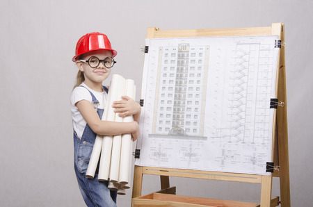 Girl Builder, architect, holding a bunch of drawings, standing at the blackboard with the drawing of the buildingの写真素材