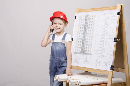 Girl playing Builder talking on the phone behind the blackboard with a drawing of a houseの写真素材