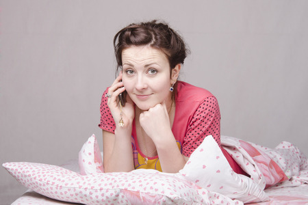 The girl lying in bed and talking on the phoneの写真素材