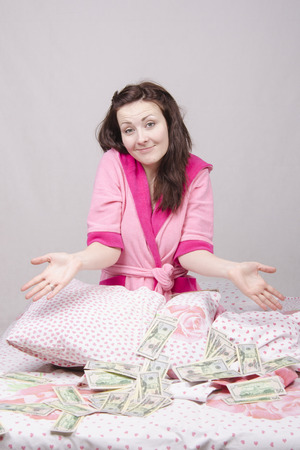 Girl sitting on the bed with a wad of bills for $ 50の写真素材