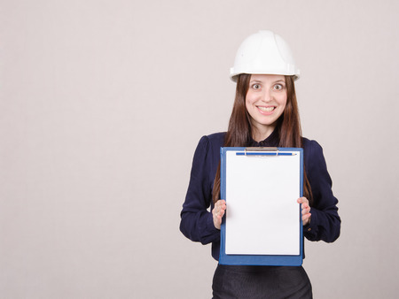 Young woman builder in helmet standing with a folder in handの写真素材