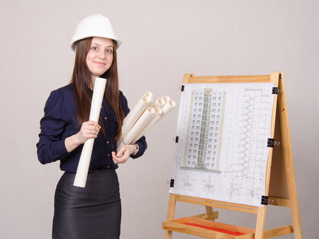 A young girl stands at the blackboard drawing multistory apartment house, in the hands of a few drawings itの写真素材