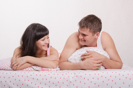 Young beautiful girl and the guy kissing and cuddling in bedの写真素材