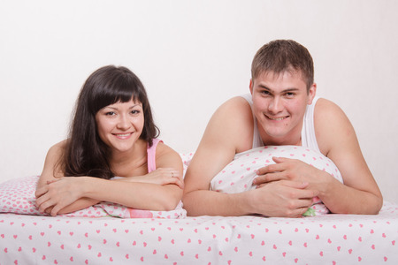 Young beautiful girl and the guy kissing and cuddling in bedの写真素材