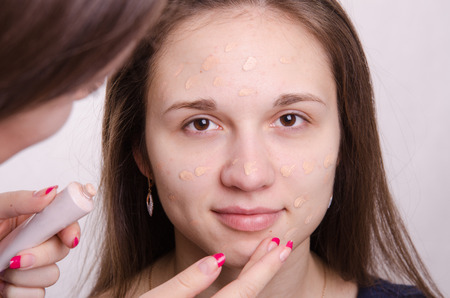 Makeup artist applies foundation of a beautiful young girl in the makeupの写真素材