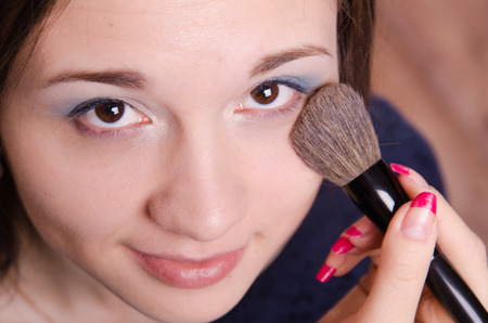 Makeup artist applies powder on the face of a beautiful young girl in the makeupの写真素材