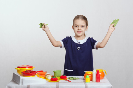 Five year old girl playing in a children's mistress dishes at a table covered with a clothの写真素材