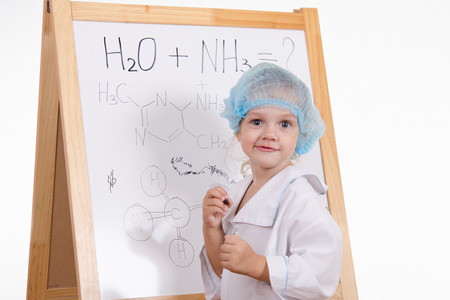 Three year old girl chemist standing at blackboard robeの写真素材