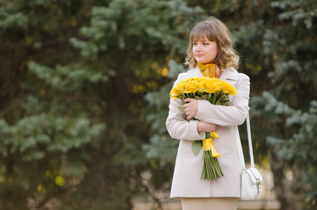 Young cute girl with a bouquet of yellow roses walks in autumn cool weatherの写真素材