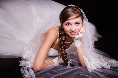 Portrait of the bride of the European type, lying on a black background in a wedding dressの写真素材