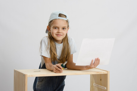 Little girl - collector of furniture with a screwdriver and instructions for assembly in the hands collects wooden cabinetの写真素材
