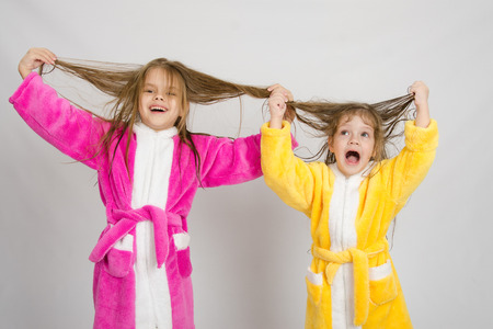 Two sister girls with wet hair standing in the bath robes on a light backgroundの写真素材