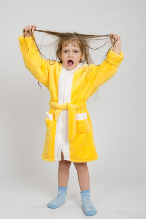 Four-year girl with wet hair in a bathrobe on a light backgroundの写真素材