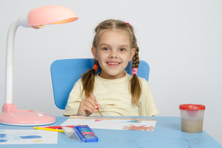 Six year old girl Europeans draws paints on a sheet of sitting at the table