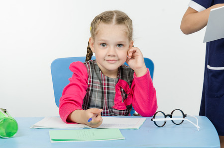 Girl sits at a table on which lay a notebook and writes them