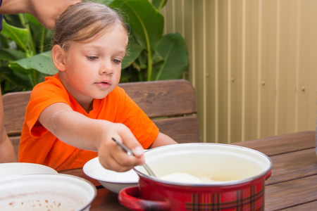 Four-year girl on breakfast imposes a ladle into a bowl semolinaの写真素材