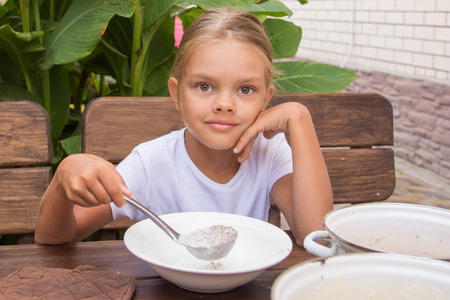 Six year old girl at breakfast imposes a ladle into a bowl buckwheatの写真素材