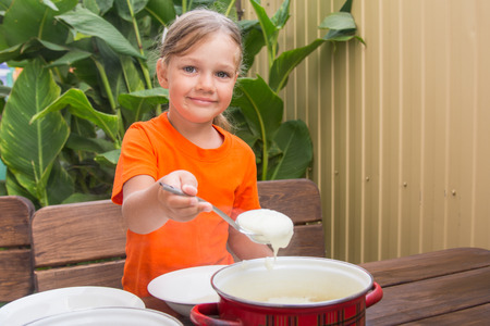 Four-year girl on breakfast imposes a ladle into a bowl semolinaの写真素材