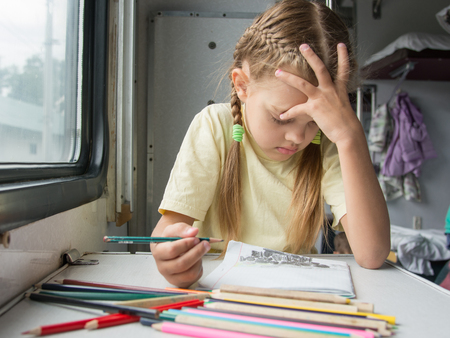 Six year old girl draws a pencil in a notebook for a side table in the second-class train carriage