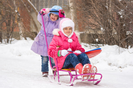 Two girls girlfriends ride each other on a sled in the snowy winter weatherの写真素材