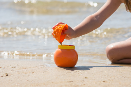 Child playing sprinkles wet sand from the molds in a pot on the sandy beach of the sea coast, close-upの写真素材