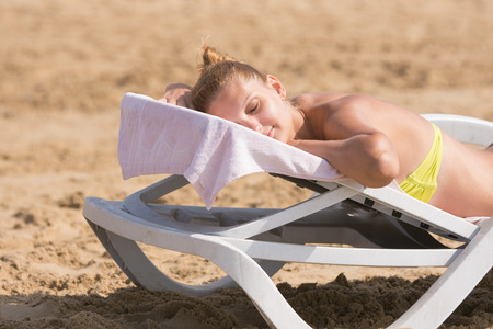 Young girl is lying on a deck chair on his stomach, his head turned and eyes closedの写真素材