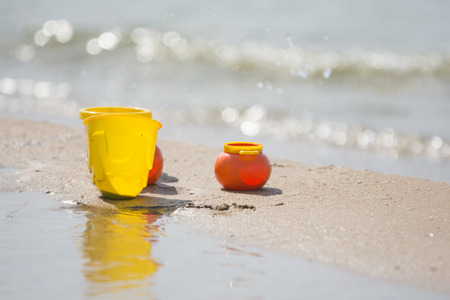 Childrens toy dishes items left on the sandy shore by the waterの写真素材