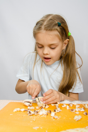 The little girl at the table with diligence knife cutting mushroomsの写真素材
