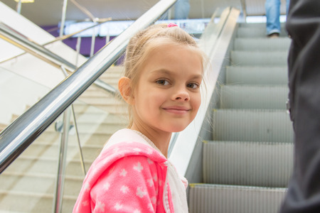 Seven-year girl lying down on an escalator in a mall with a smile look in the frameの写真素材