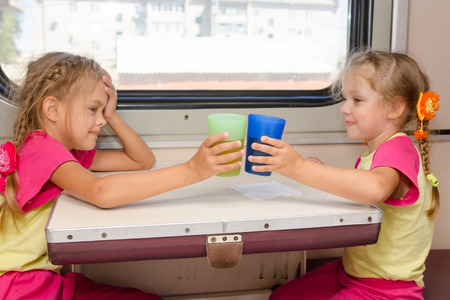 Two little sisters in identical pajamas drinking tea in the train at the table on outboard second-class carriageの写真素材