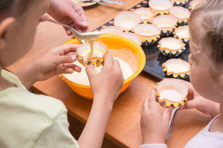 Two girls helped mom to pour batter into the molds for cupcakesの写真素材