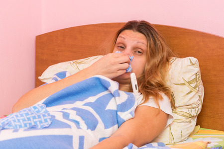 Young girl coughing heavily lying in bedの写真素材