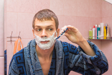 Young man shaves the stubble on his cheekの写真素材