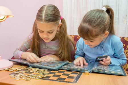 Two children studying coins in albumの写真素材
