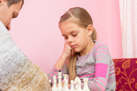 Seven-year daughter is thinking about the next move, playing chessの写真素材