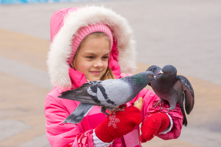 girl in a pink jacket watching the pigeons that sit on her hands